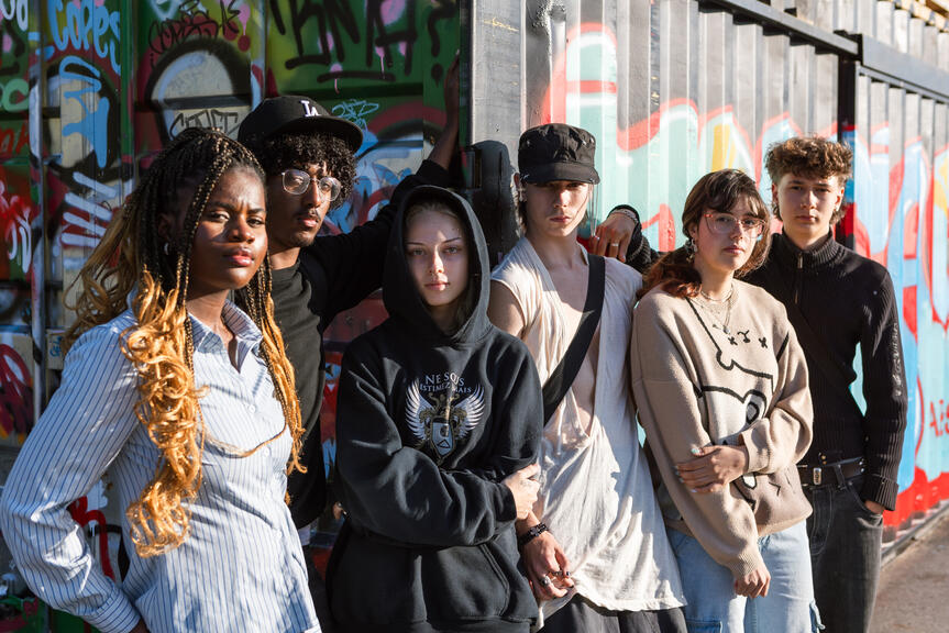 Group of young people standing in front of a graffiti wall.