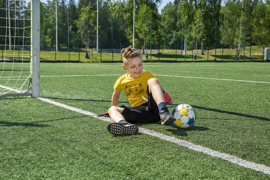A child is sitting with a football beside them on a sunny outdoor field.