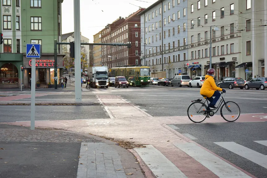 Suurten katujen risteys, jossa on pyöräilijä ja autoja liikennevaloissa
