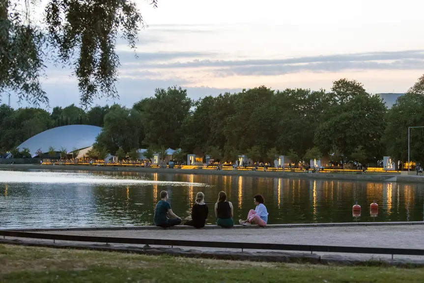Neljä ihmistä istumassa Eläintarhanlahden rannalla iltahämärässä