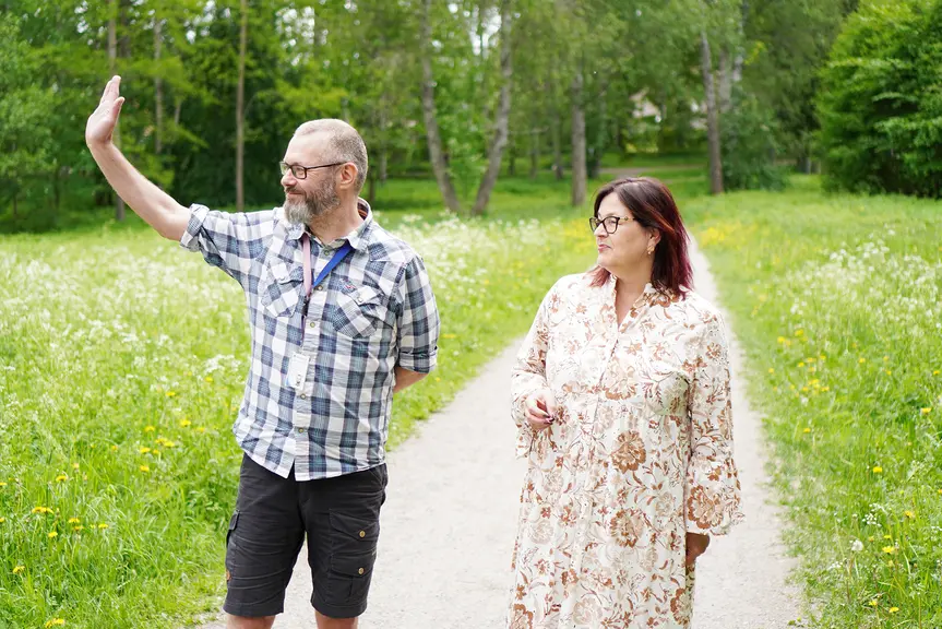 Juhani ja Jaana puistotiellä. Juhani vilkuttaa työkaverille.