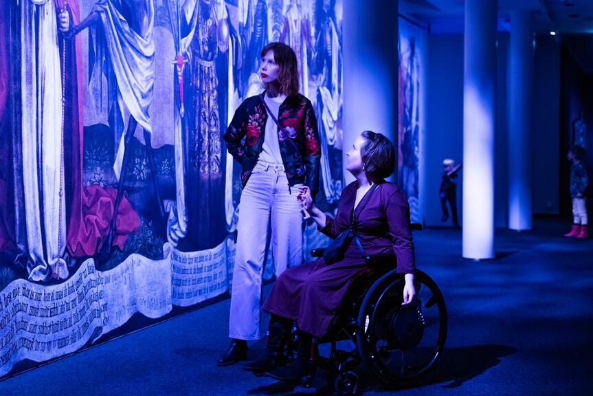 Two people looking at art hanging on a wall in a blue-tinted room.