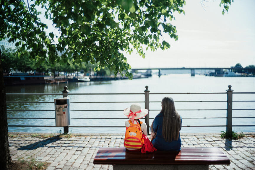 Nainen ja lapsi istuvat penkillä veden äärellä