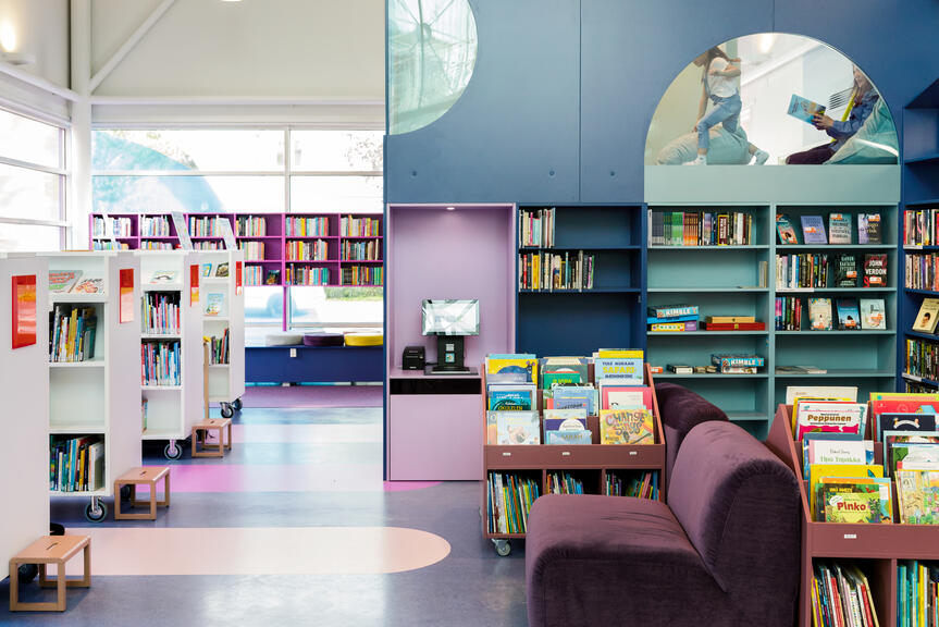 Blåtonade bokhyllor och en läsloft i Lillhoplax barnbiblioteks biblioteksal.