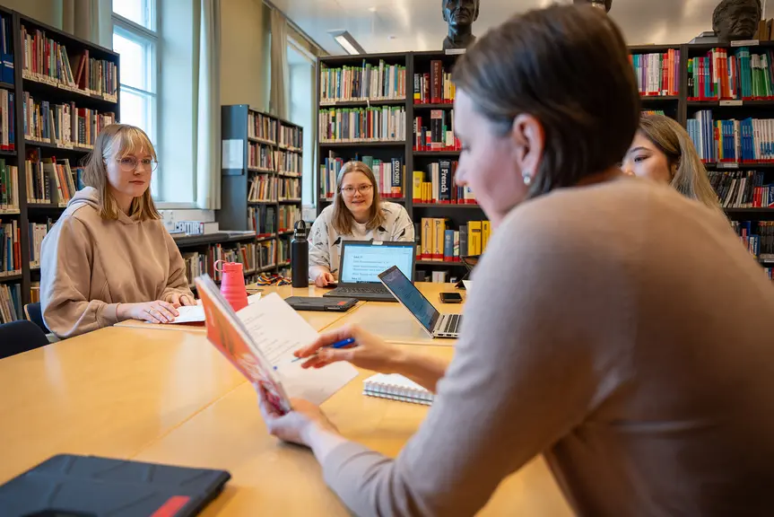 Opiskelijat ja opettaja keskustelevat kirjasta pöydän ääressä