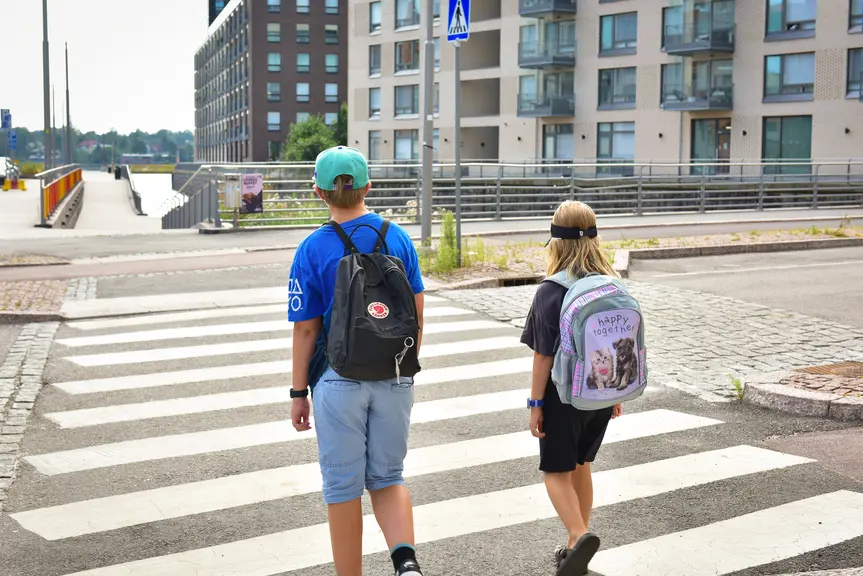 Kaksi lasta ylittämässä tietä suojatiellä.