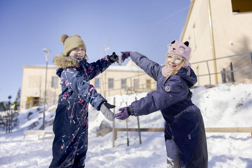 Kaksi lasta talvivaatteissa lumisella pihalla.