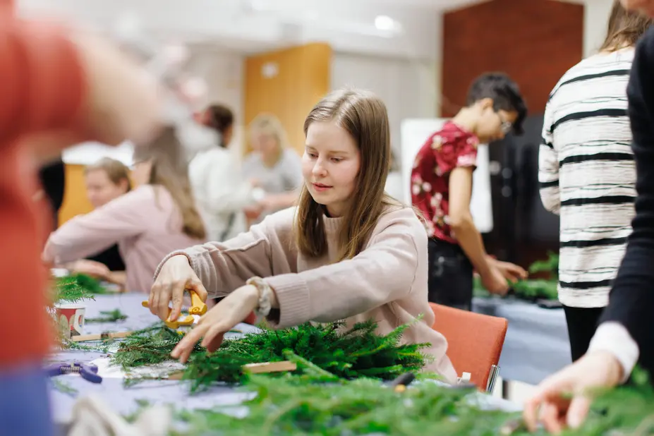 Henkilö askartelee joulukranssia.