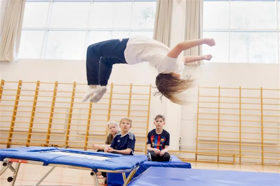 Lapsi hyppää voltin trampoliinilla.