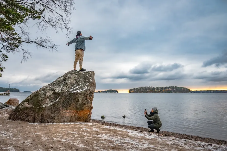 Henkilö kuvaa toista henkillö kivellä, taustalla meri.