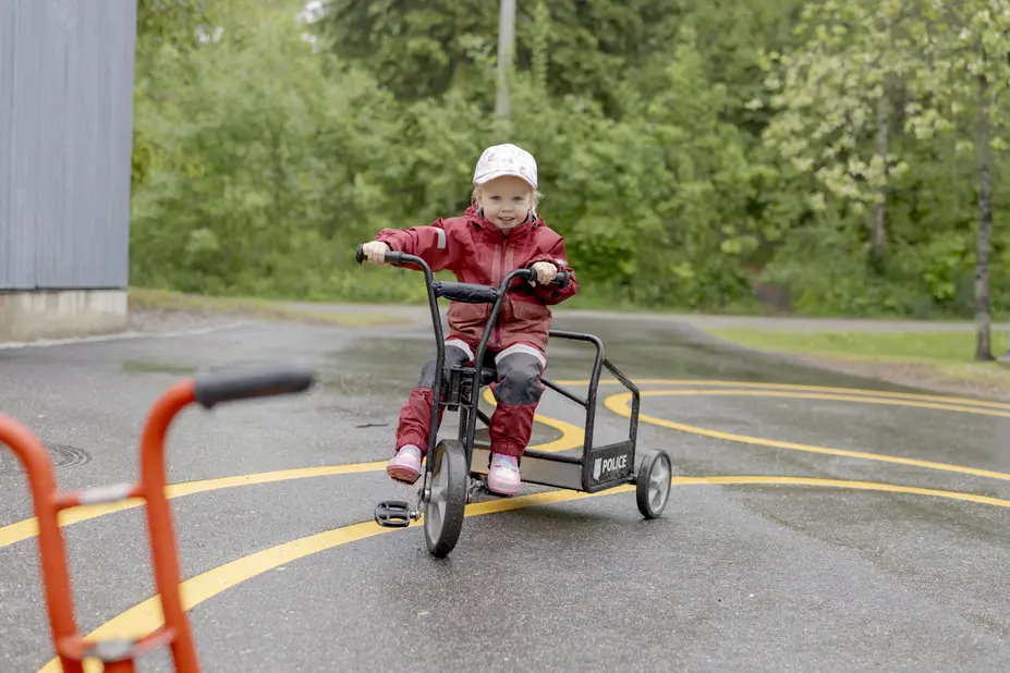 Lapsi pyöräilee leikkipuiston pihalla.