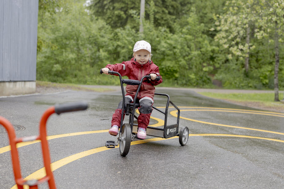 Lapsi pyöräilee leikkipuiston pihalla.