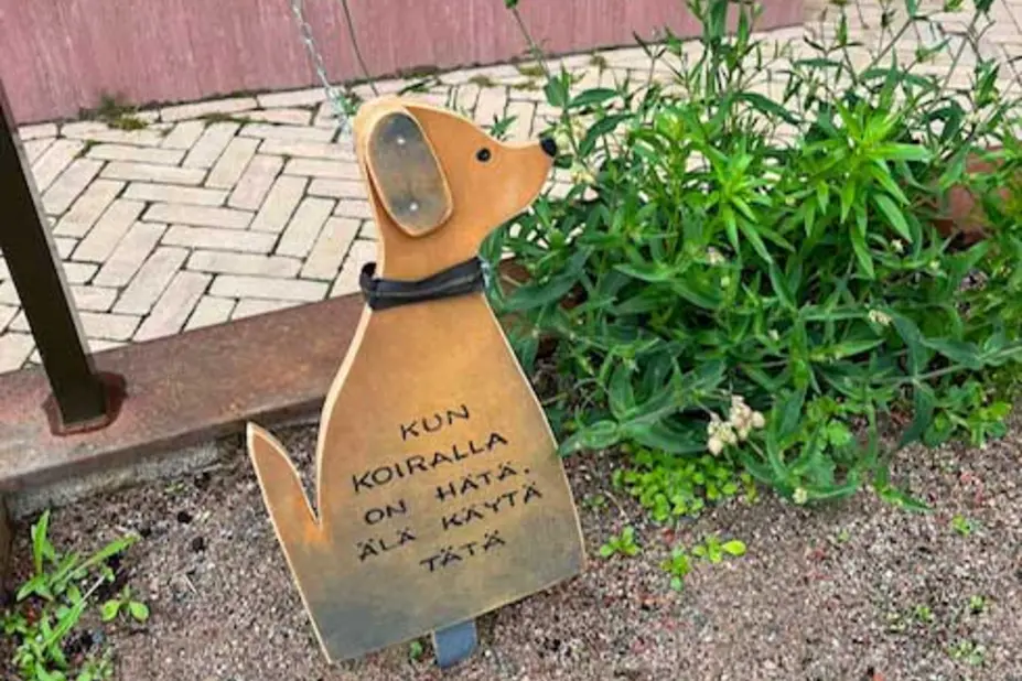 Koiranmuotoinen kyltti kukkapenkissä.