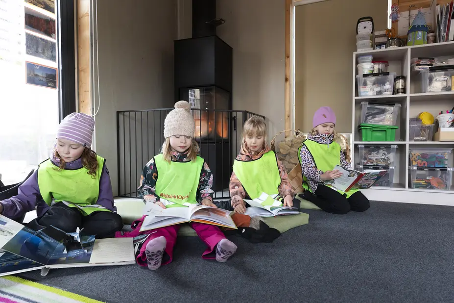 Neljä lasta istuu ulkovaatteissa kodan lattialla ja lukee kirjoja