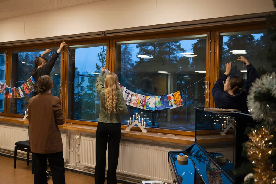 Metropolia-ammattikorkeakoulun opiskelijat ripustavat värikkäitä lyhtyjä seniorikeskuksen ikkunoihin.
