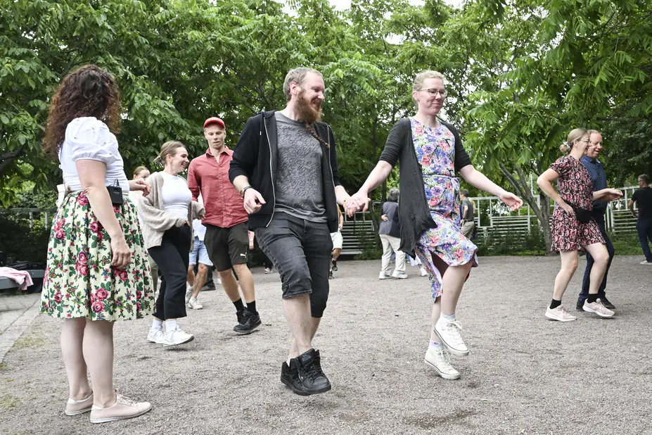 Leende människor dansar pardans på Malms kulturhus grönskande gård. En kvinna står och tittar på dem.