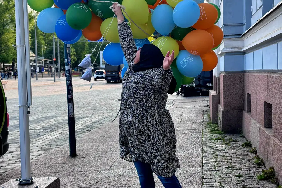 Woman jumps for joy with balloons in front of City Hall