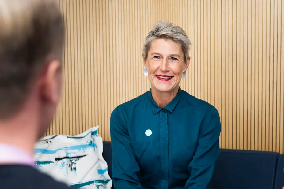  Chefen för Tölö seniorcenter Pia-Maria Grönqvist sitter på en soffa och ler.