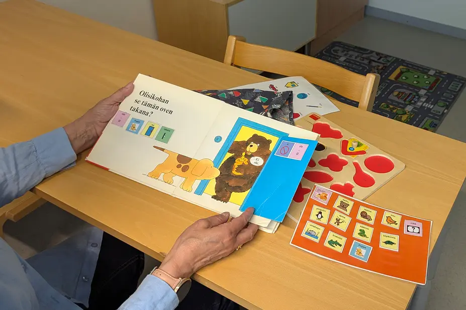 Puheterapeutilla on kädessä lastenkirja, jota käytetään arviointivälineenä.