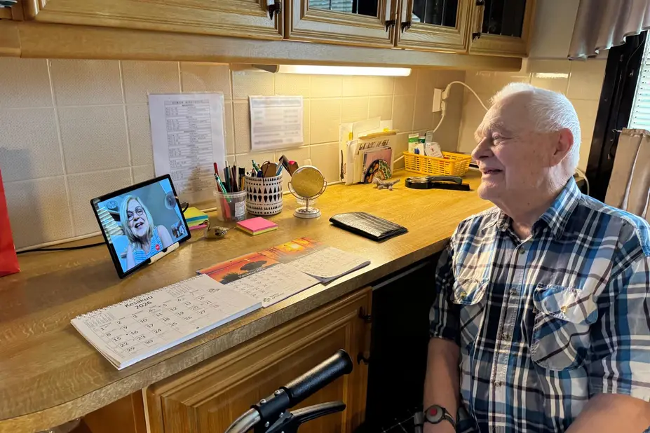 Iäkäs mies istuu tabletin äärellä videopuhelussa tyttärensä kanssa