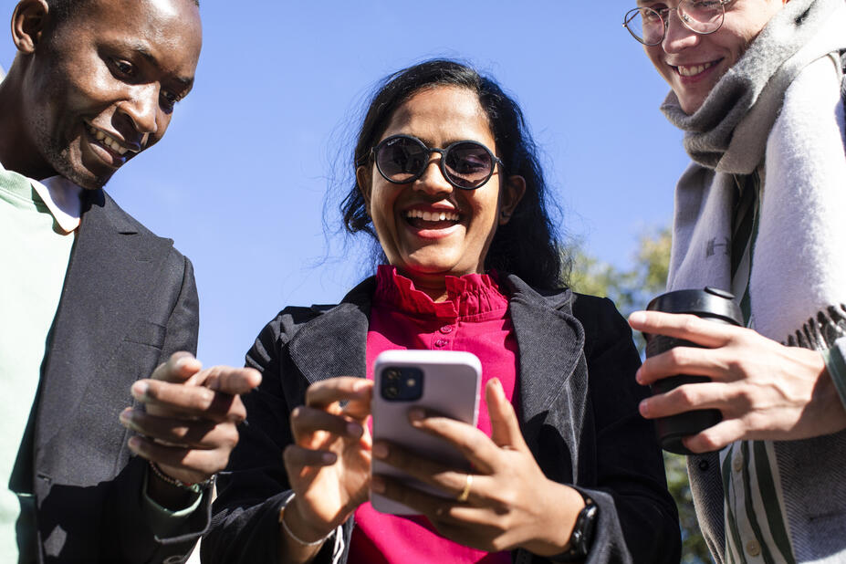 Three people looking at a mobile phone together and smiling.