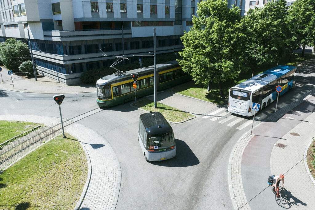 Minibussi, linja-auto ja raitiovaunu risteyksessä kesällä.