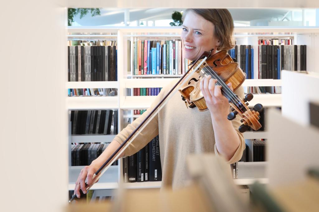A woman plays the violin in front of the bookshelves in the library