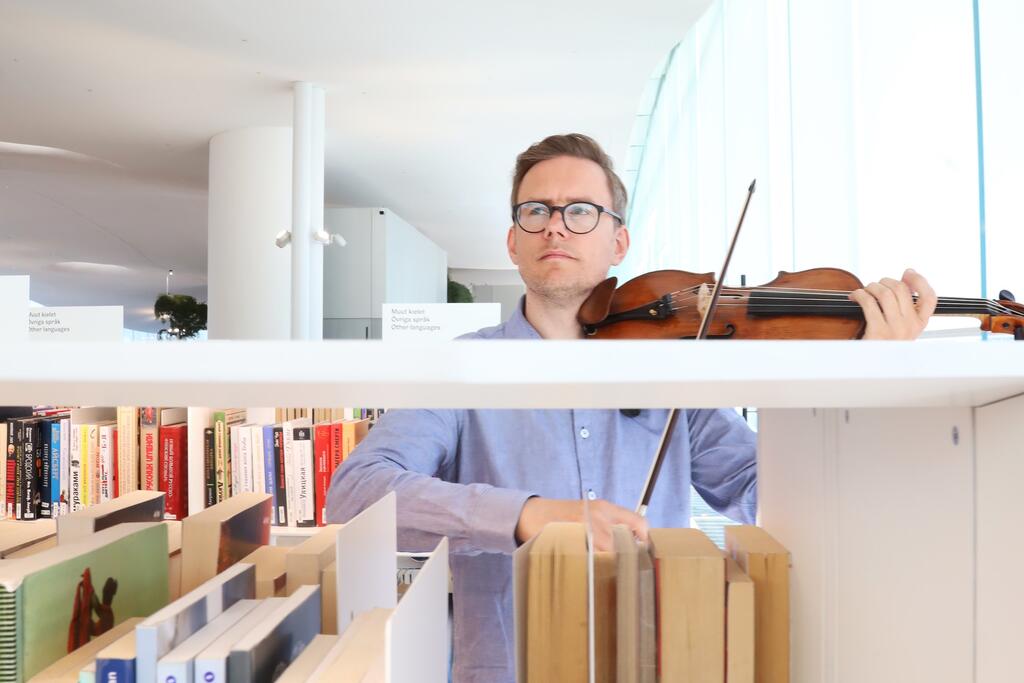 A man plays the violin between the bookshelves in the library.