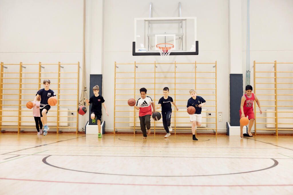 Група дітей грає в баскетбол у шкільному спортзалі.