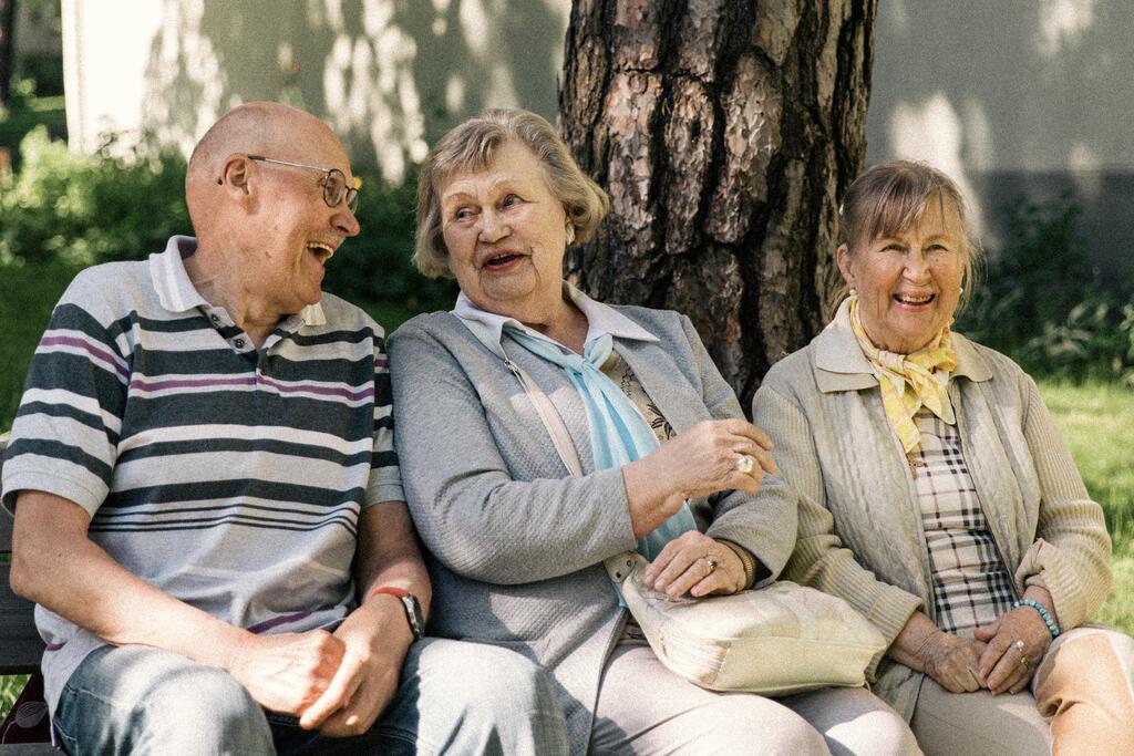 Three elderly persons sit on a bench in a courtyard.
