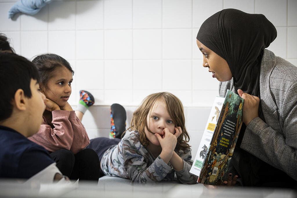 Lapset kuuntelevat keskittyneesti, kun Kafeya Mohamed lukee heille satua. Välillä kysytään ja keskustellaan. Kuva: Antti Nikkanen