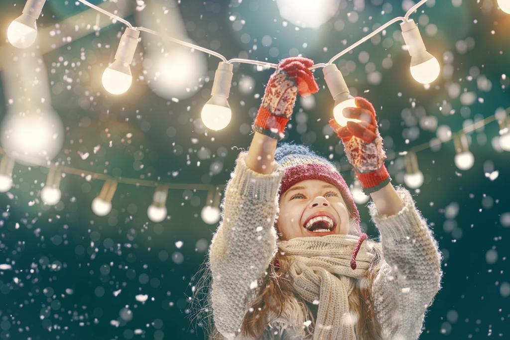 Tyttö ripustaa jouluvaloja lumisateessa