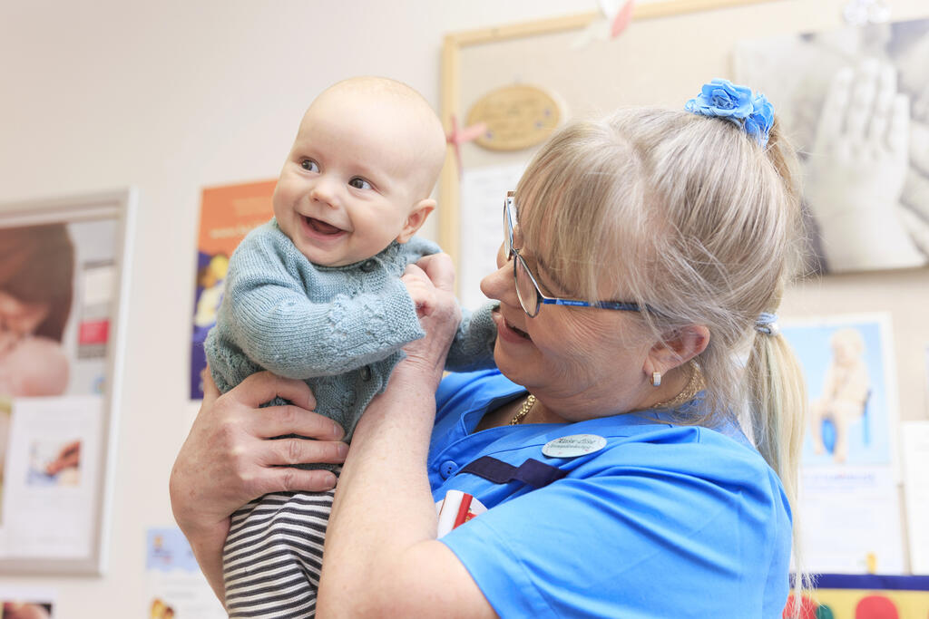 Neuvolan terveydenhoitaja pitää sylissä hymyilevää vauvaa