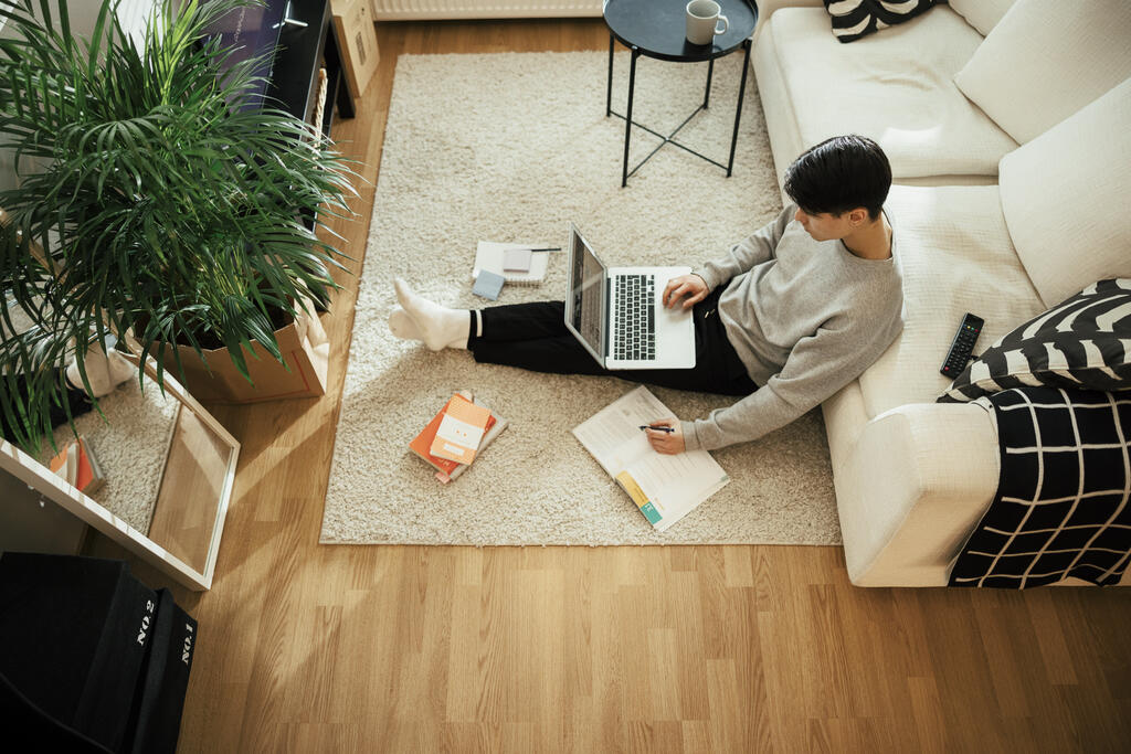 Nuori mies istuu olohuoneen lattialla rennossa asennossa tietokone sylissä