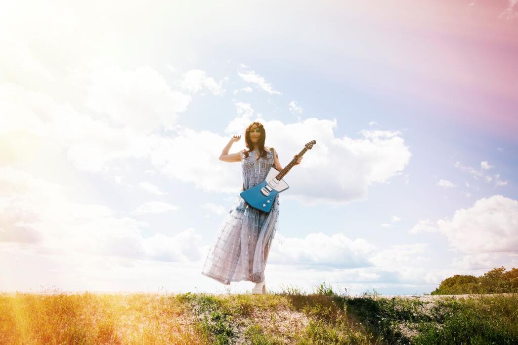 The red-haired woman standing in the sunshine with a guitar in her hand. 