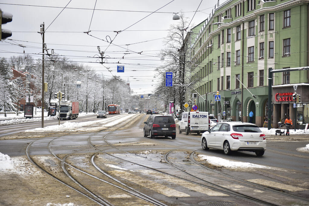 Mannerheimintie Oopperan risteyksessä helmikuussa 2023. Kadulla hieman lunta ja autoja. Puissa lunta, taivas harmaa.