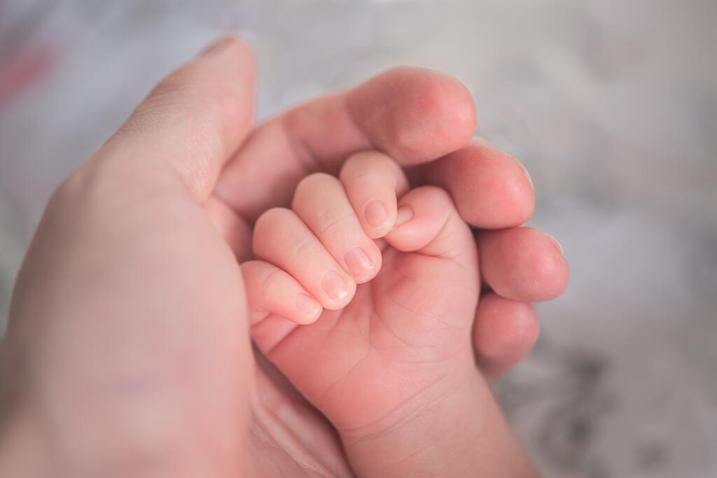 Aikuisen käsi pitää kiinni vauvan kädestä