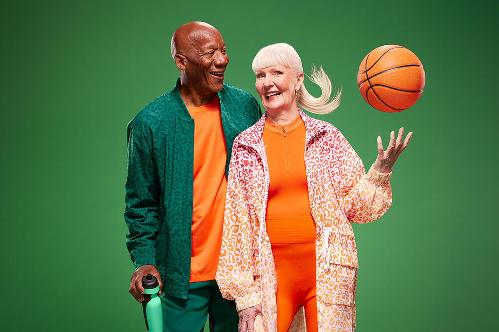 A smiling man looks at a woman throwing a basketball into the air.