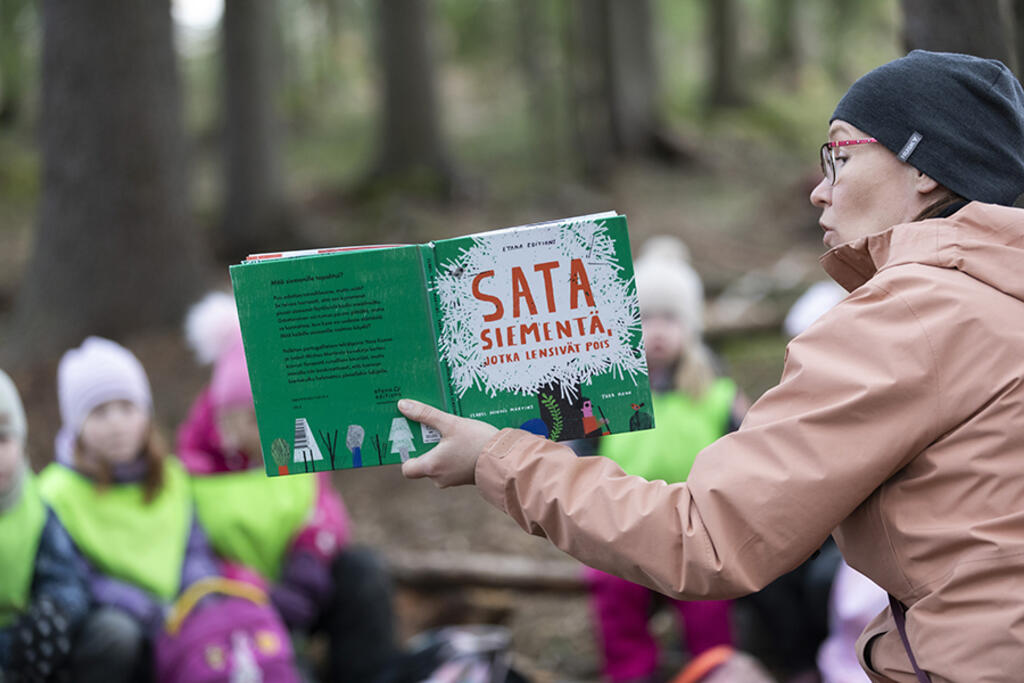 Eeva Koskela lukee metsässä lapsille kirjaa.