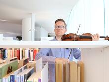 Mies soittaa viulua kirjaston kirjahyllyjen välissä.
