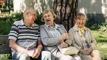 Kolme hymyilevää ikäihmistä istuu pihapenkillä.