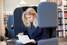 Opiskelija selaa muistiinpanojaan kirjaston tuolissa