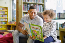 Aikuinen ja lapsi lukemassa kirjaa kirjastossa.