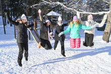 Opettaja ja neljä oppilasta hyppäävät ilmaan talvisessa leikkipaikka Tuhkimossa.