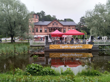 Kuvassa Oulunkylän Seurahuone ja edustalla telttoja ja ihmisiä sekä Ogelin kyläjuhla -lippu.