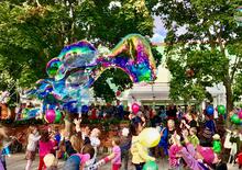 Iso joukko lapsia leikkii värikkäillä ilmapalloilla ja saippuakuplilla.