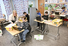 Oppilaita ja opettaja koululuokassa kannettavien tietokoneiden äärellä.