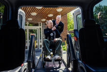 Kuljettaja avustaa pyörätuolissa istuvaa henkilöä inva-auton kyytiin.