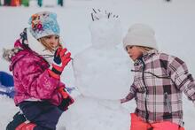 Kaksi lasta rakentaa lumiukkoa