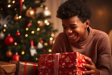 Nuori lahjapaketin kanssa joulukuusen äärellä